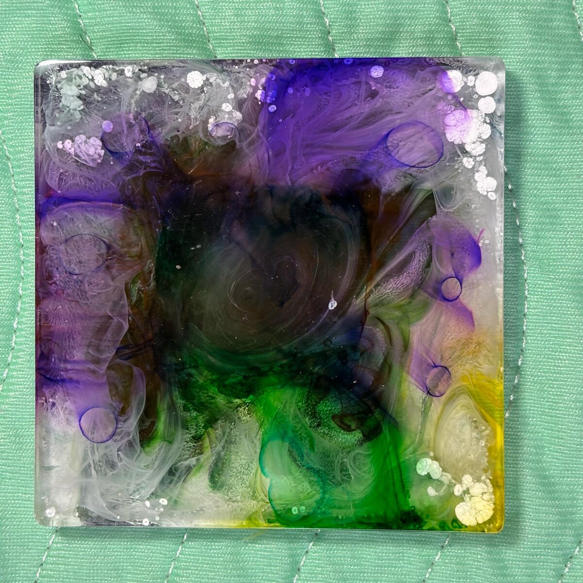 Square resin coaster with purple, green, white, and yellow floral-like movement