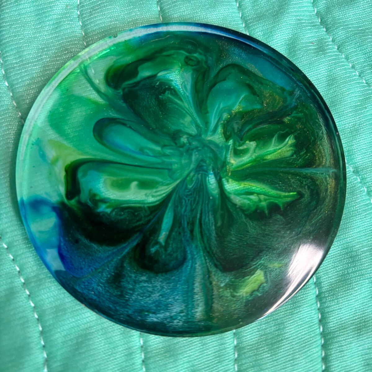 Round teal resin coaster with flower-like blue and green pattern